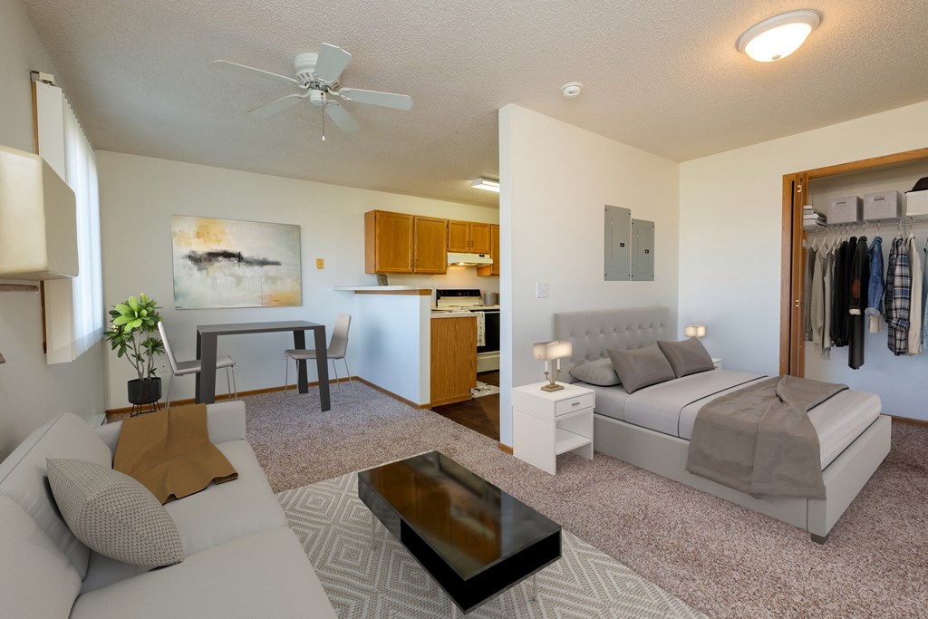 a studio apartment furnished with a couch, bed, dining table, with a kitchen in the background. Fargo, ND Bridgeport Apartments