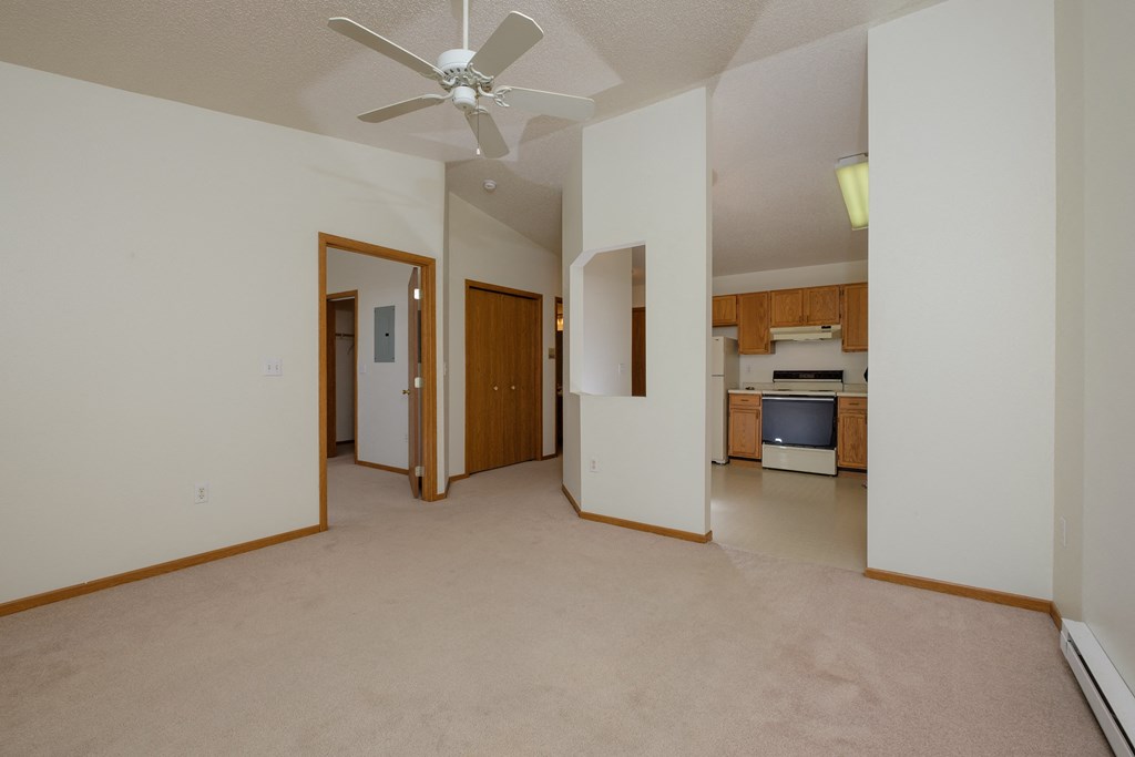 a living room with a ceiling fan and a kitchen in the background. Fargo, ND Bridgeport Apartments