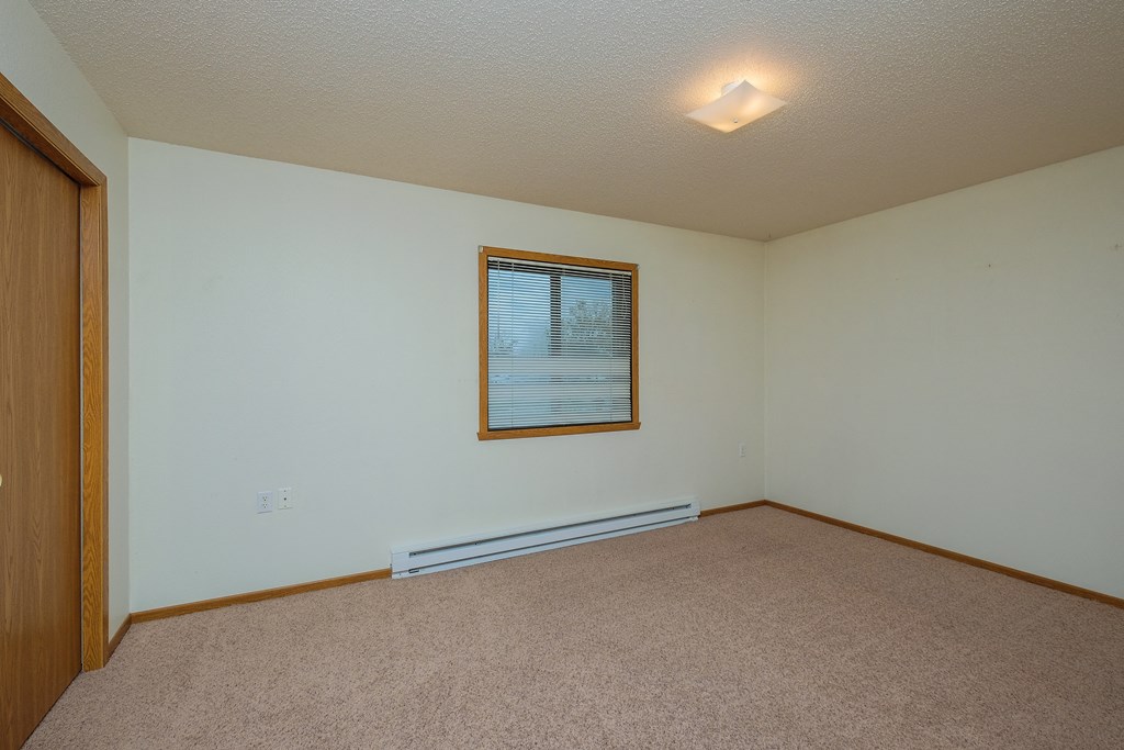 a bedroom with a window and a carpeted floor. Fargo, ND Bridgeport Apartments