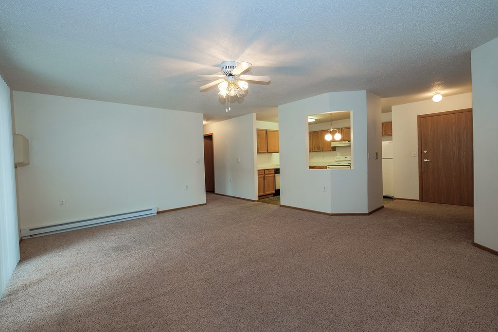a living room with a ceiling fan and a kitchen in the background. Fargo, ND Bridgeport Apartments