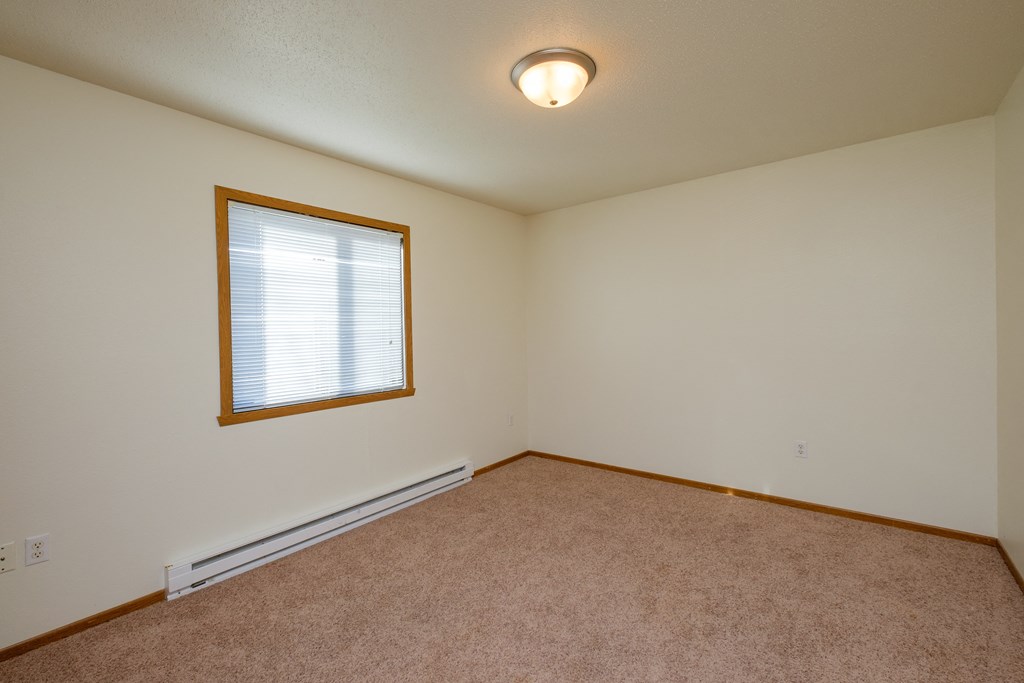 a bedroom with a window and a carpeted floor. Fargo, ND Bridgeport Apartments