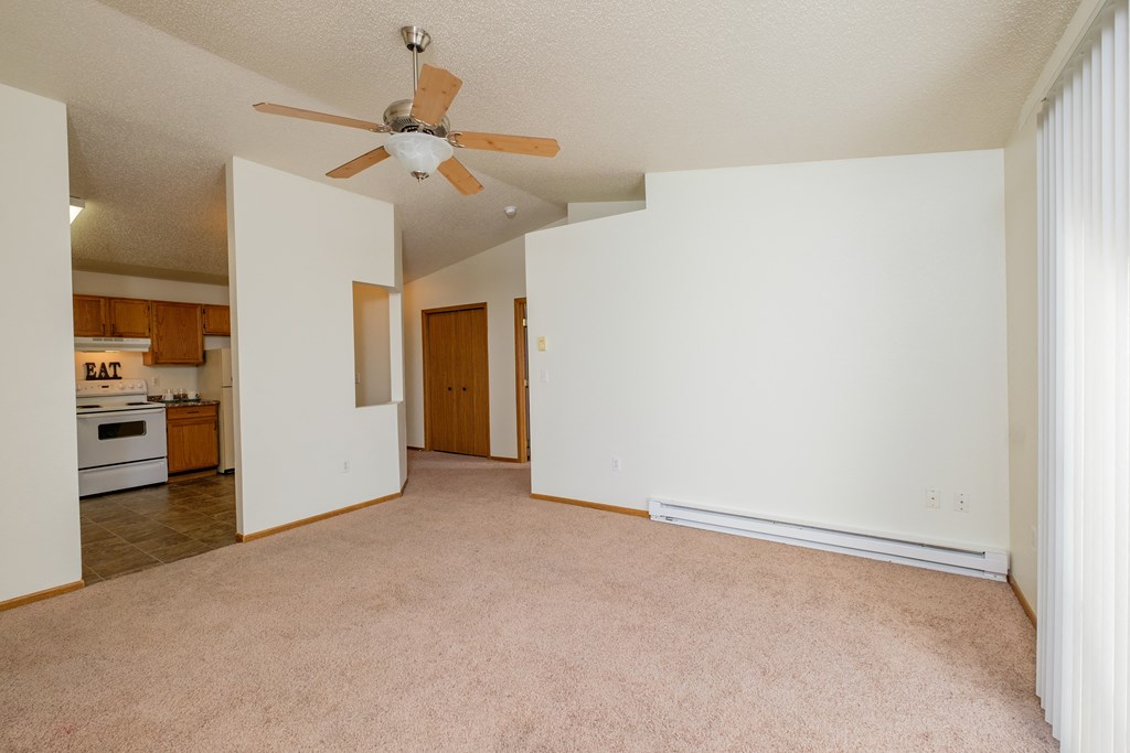 a living room with a ceiling fan and a kitchen in the background. Fargo, ND Bridgeport Apartments