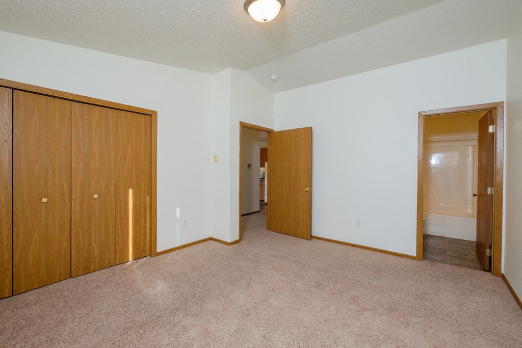 a master bedroom with a bathroom attached and a closet. Fargo, ND Bridgeport Apartments