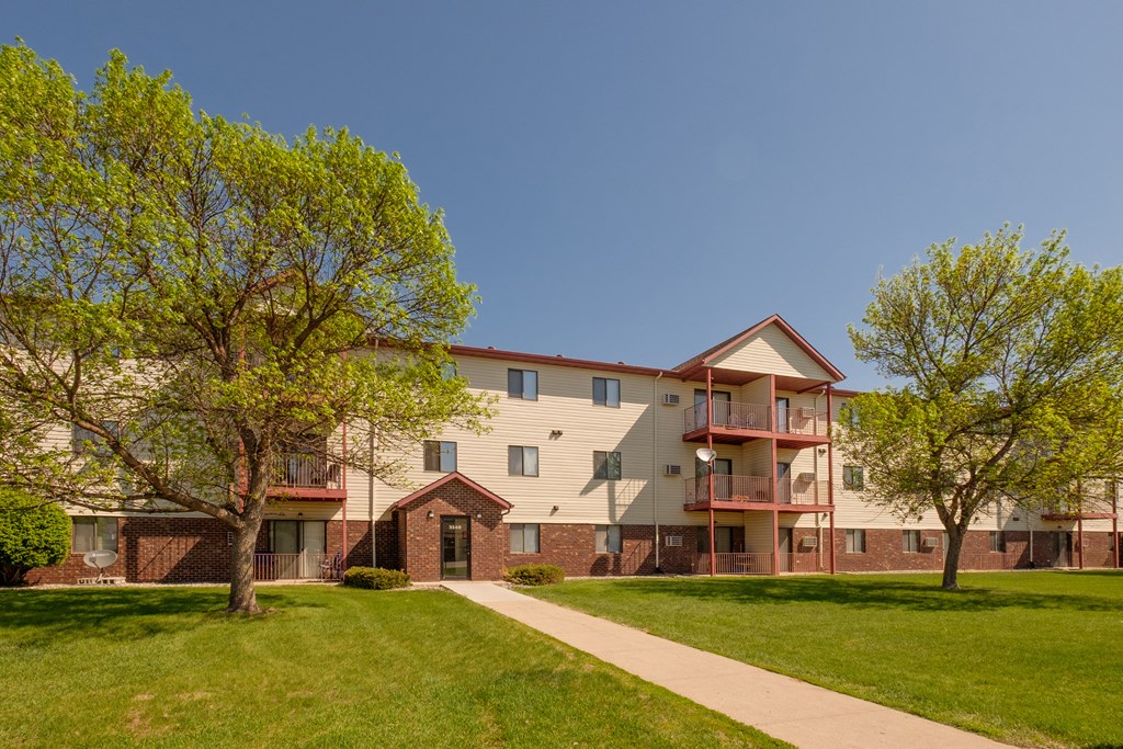 the outside of an apartment building with three levels and two trees. Fargo, ND Bridgeport Apartments