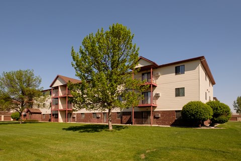 the outside of a three level apartment building with two trees out front. Fargo, ND Bridgeport Apartments