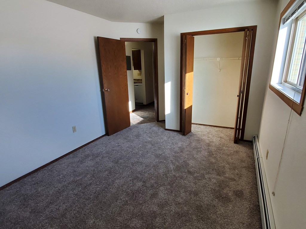 an empty room with a carpeted floor and a door to a closet. Fargo, ND Brookfield Apartments