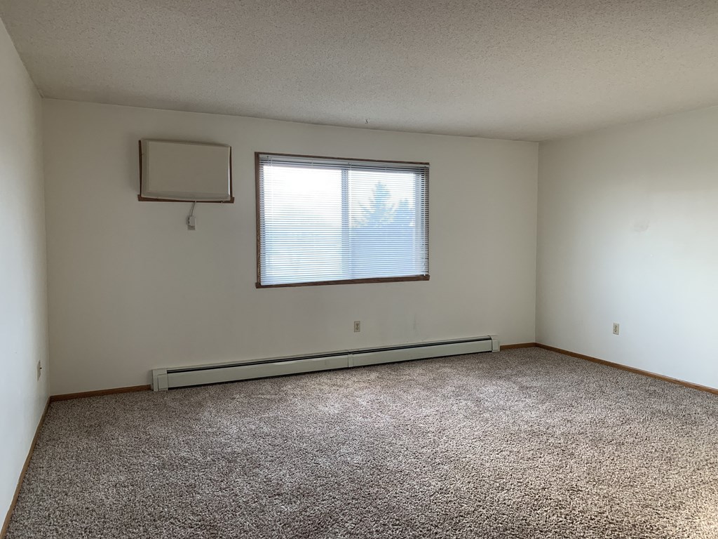 an empty living room with a window and carpet. Fargo, ND Brookfield Apartments