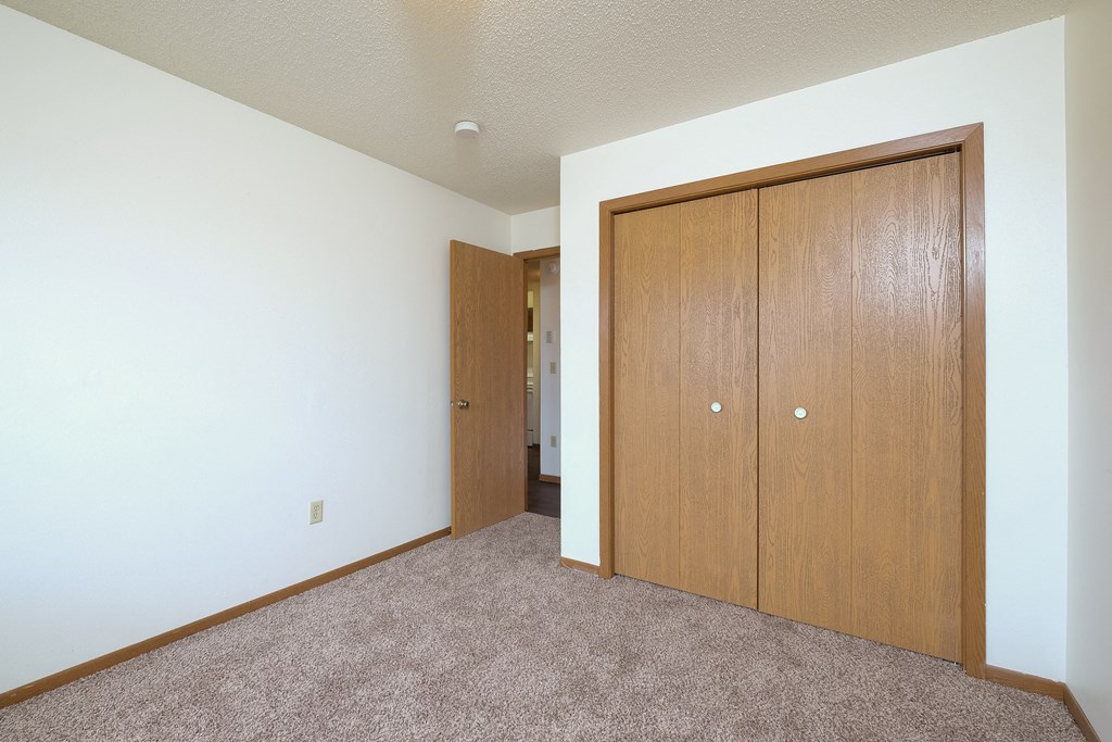 a bedroom with a closet and a door to a hallway. Fargo, ND Carlton Place Apartments
