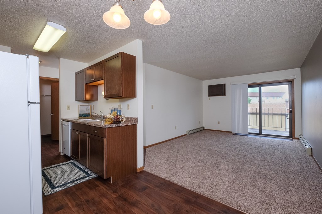 an empty living room with a kitchen and a door to a balcony. Fargo, ND Carlton Place Apartments