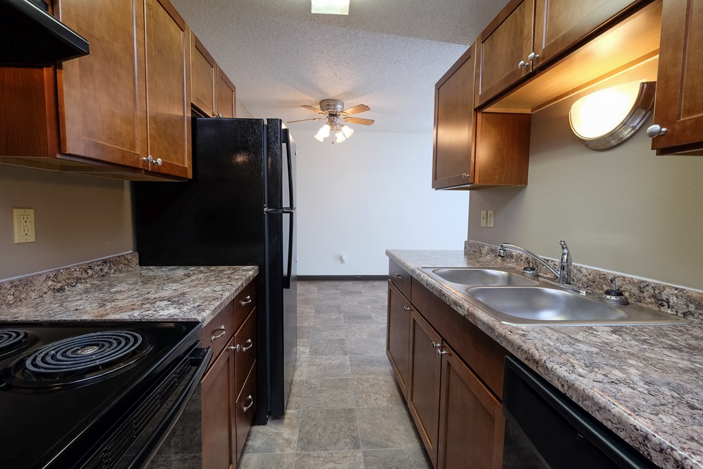 a kitchen with black appliances and granite counter tops and wooden cabinets. Fargo, ND Carlton Place Apartments