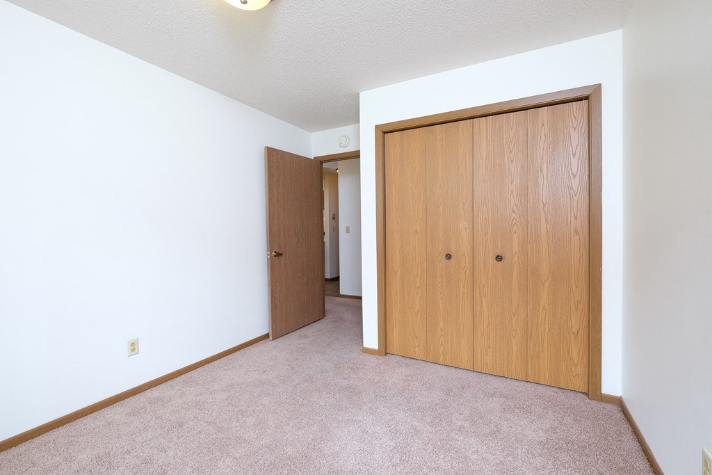 a bedroom with a closet and a door to a hallway. Fargo, ND Carlton Place Apartments
