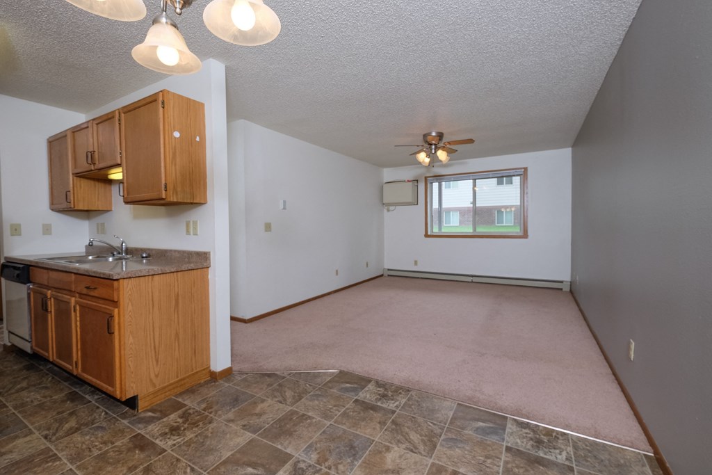 an empty living room with a kitchen and a ceiling fan. Fargo, ND Carlton Place Apartments