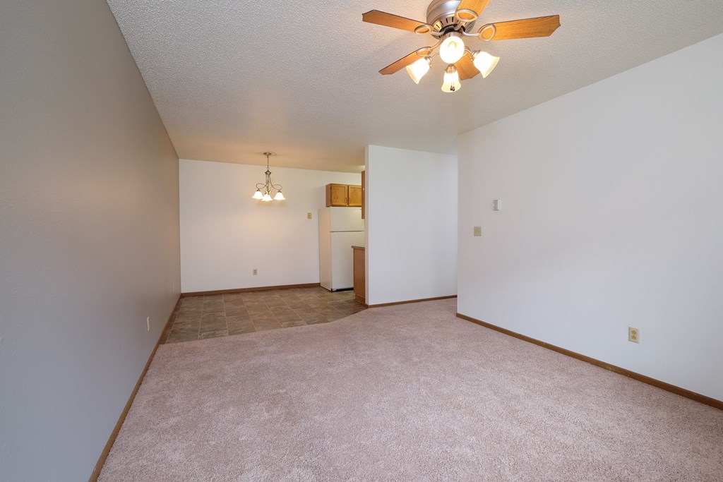 an empty living room with a ceiling fan and white walls. Fargo, ND Carlton Place Apartments