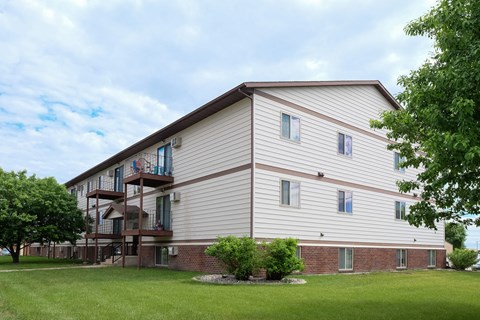 the exterior of a building with a green lawn and trees. Fargo, ND Carlton Place Apartments
