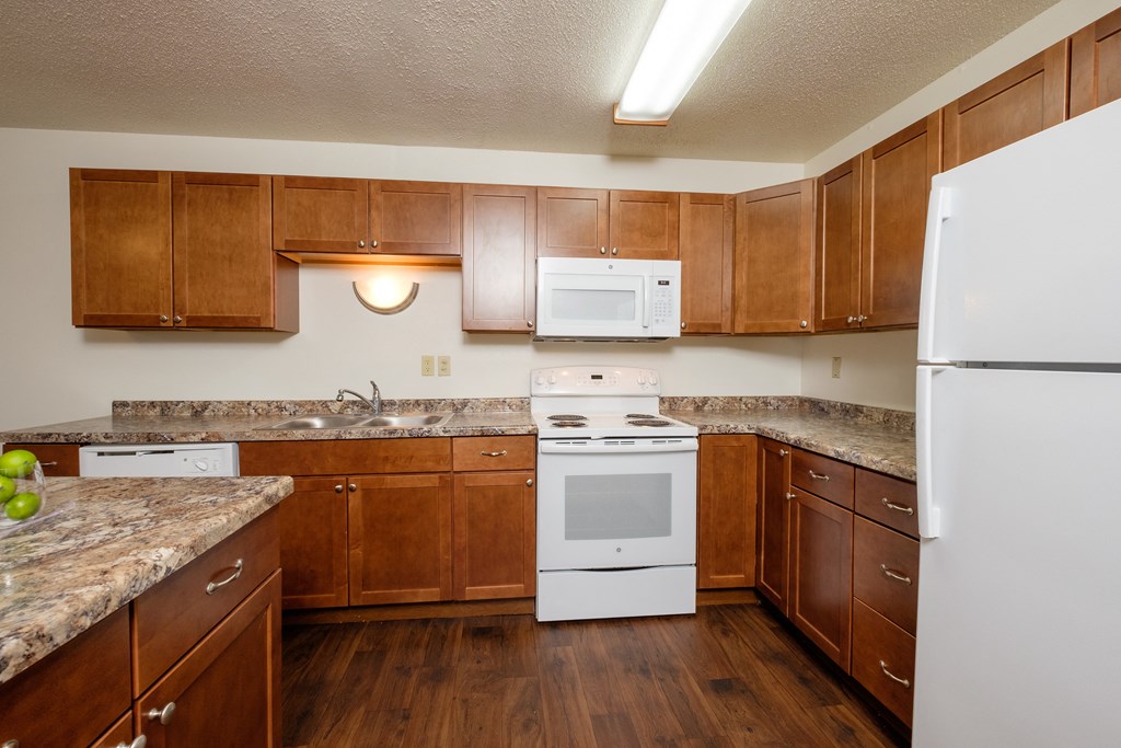 a kitchen with white appliances and wooden cabinets. Fargo, ND Cedars 2 Apartments