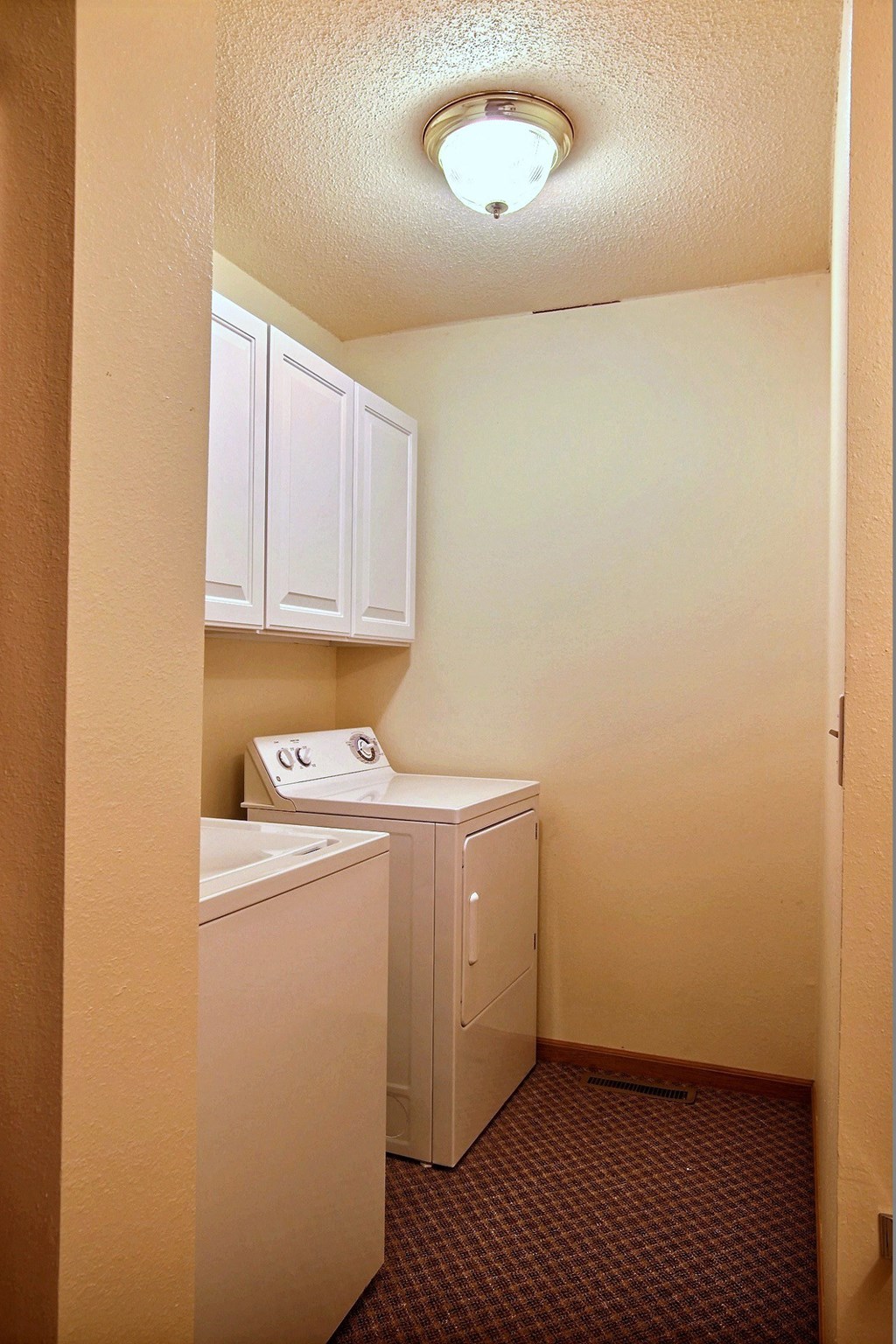 A small laundry room with a washer and dryer and white cabinets