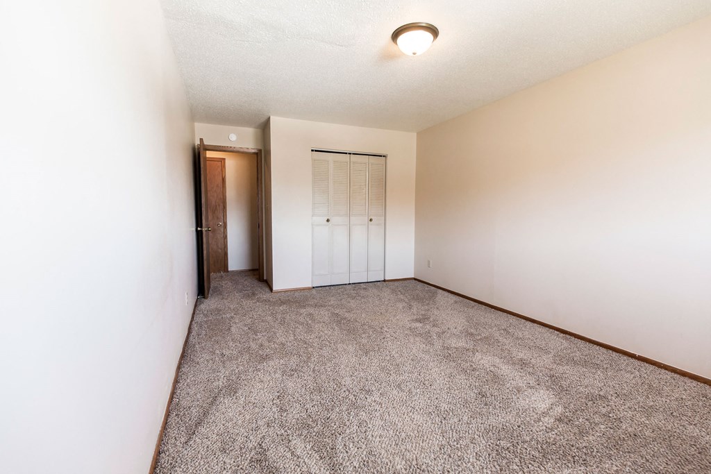Grand Forks, ND Cherry Creek Apartments. A bedroom in unit 223 that has a window, white walls, a closet, and carpeted floors