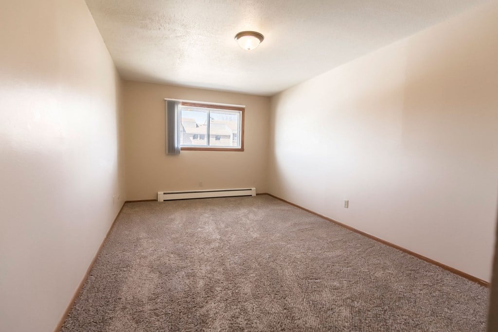 Grand Forks, ND Cherry Creek Apartments. A bedroom in unit 223 that has a window, white walls, and carpeted floors