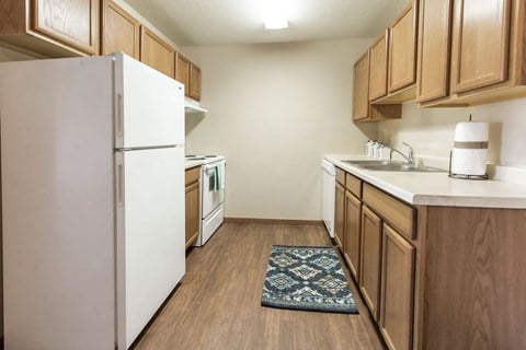 Grand Forks, ND Cherry Creek Apartments. A kitchen with a rug by the sink and white appliances.