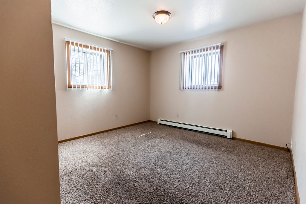 Grand Forks, ND Cherry Creek Apartments. A bedroom with a closet, 2 windows, white walls, and carpeted floors