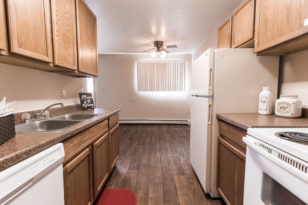 Grand Forks, ND Cherry Creek Apartments. A kitchen in the unit 110 with wood floors an white appliances with a dining room in the background that has a window
