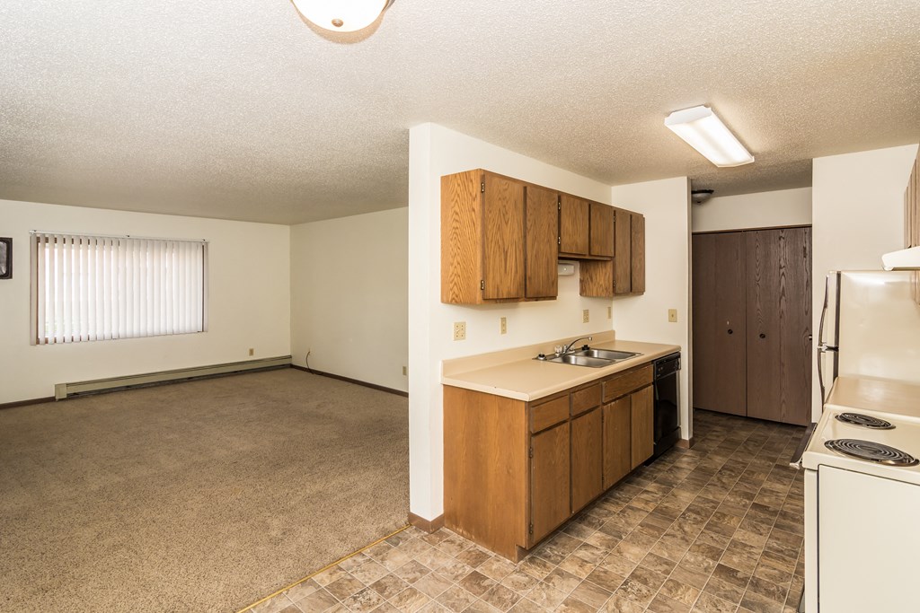 Grand Forks, ND Columbia West Apartments. A kitchen with white appliances and a living room with a window in the background.