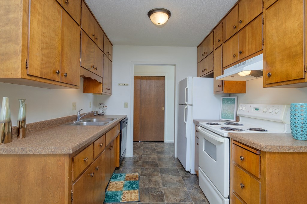 a kitchen with white appliances and wooden cabinets. Fargo, ND Country Club Apartments.