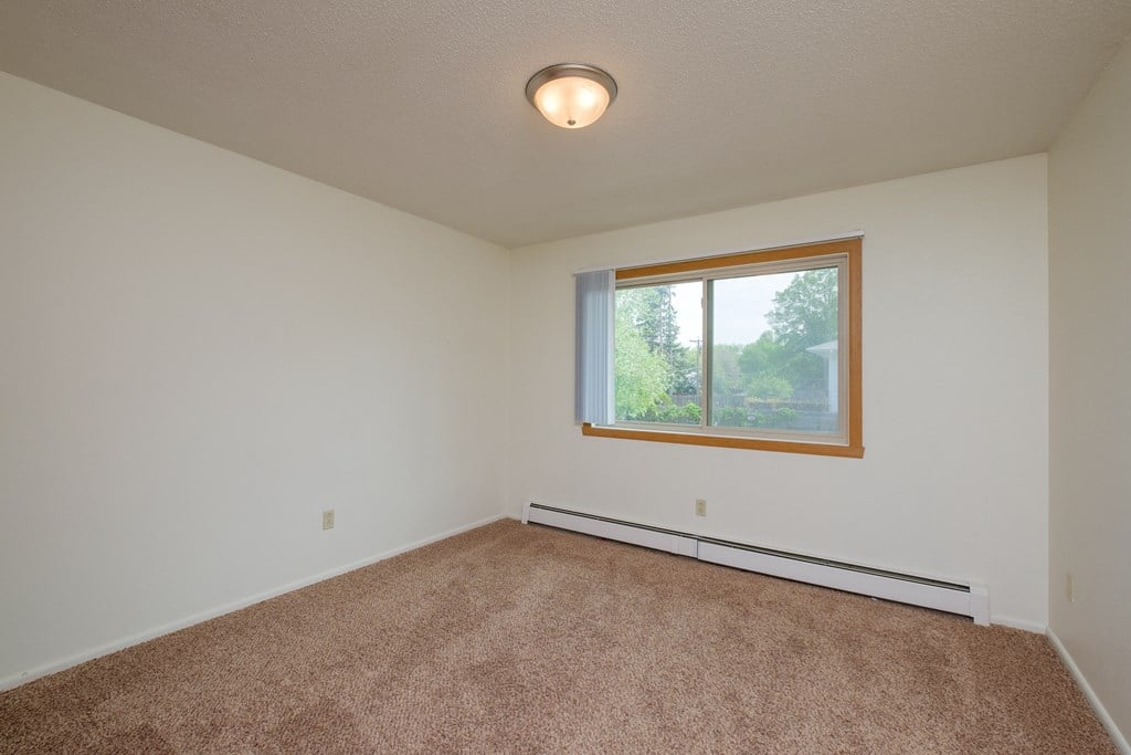an empty living room with carpet and a window. Fargo, ND Country Club Apartments.