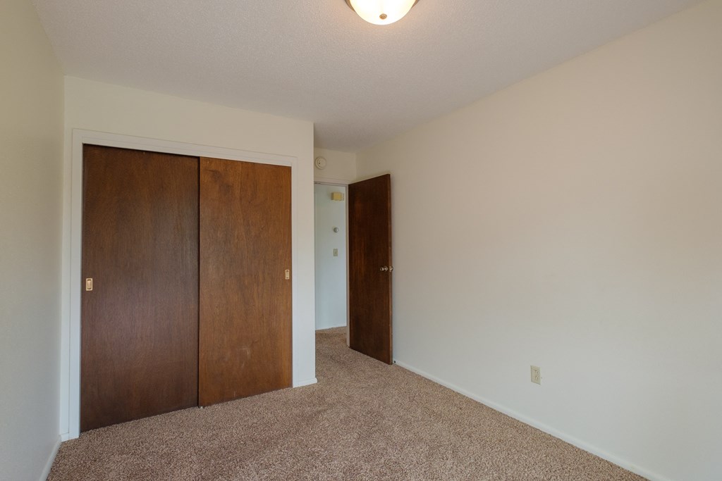 a bedroom with a closet and a door to a hallway. Fargo, ND Country Club Apartments.