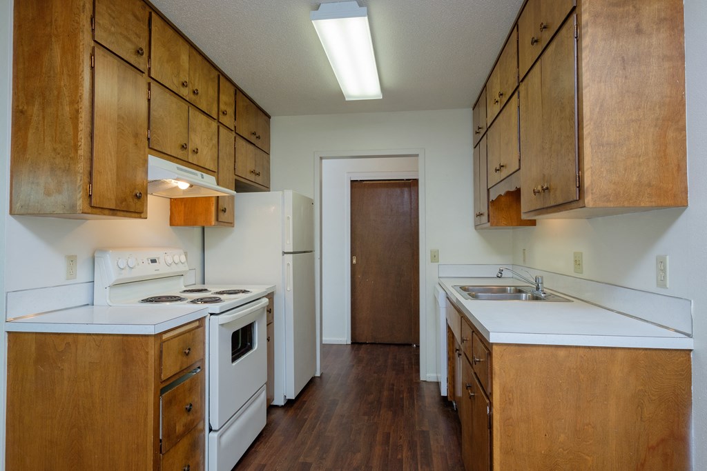 an empty kitchen with white appliances and wooden cabinets. Fargo, ND Country Club Apartments.