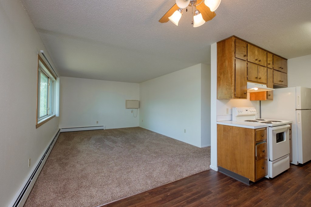 an empty living room with a kitchen with a stove and refrigerator. Fargo, ND Country Club Apartments.