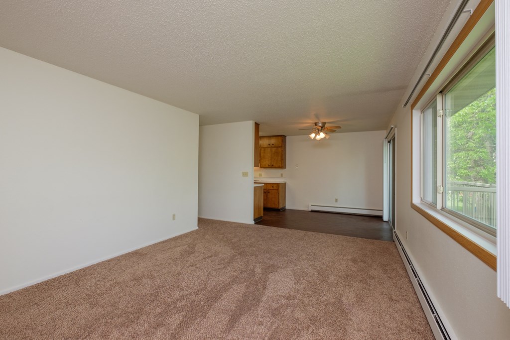 an empty living room with a large window and carpet. Fargo, ND Country Club Apartments.