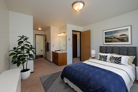 a bedroom with a large bed and a potted plant. Fargo, ND Countryside Apartments