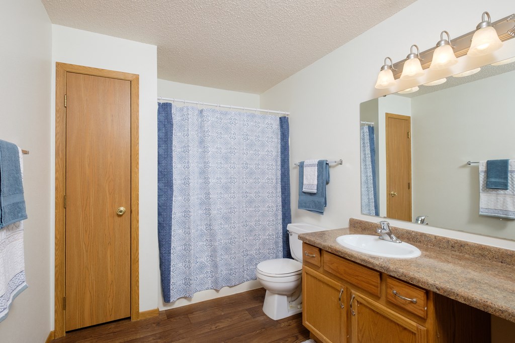 a bathroom with a shower and a toilet and a sink. Fargo, ND Danbury Apartments