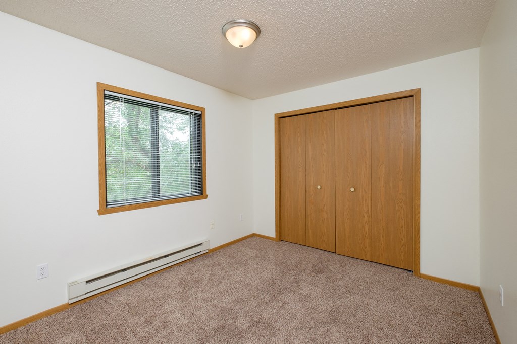 a bedroom with carpet and a door to a closet. Fargo, ND Danbury Apartments