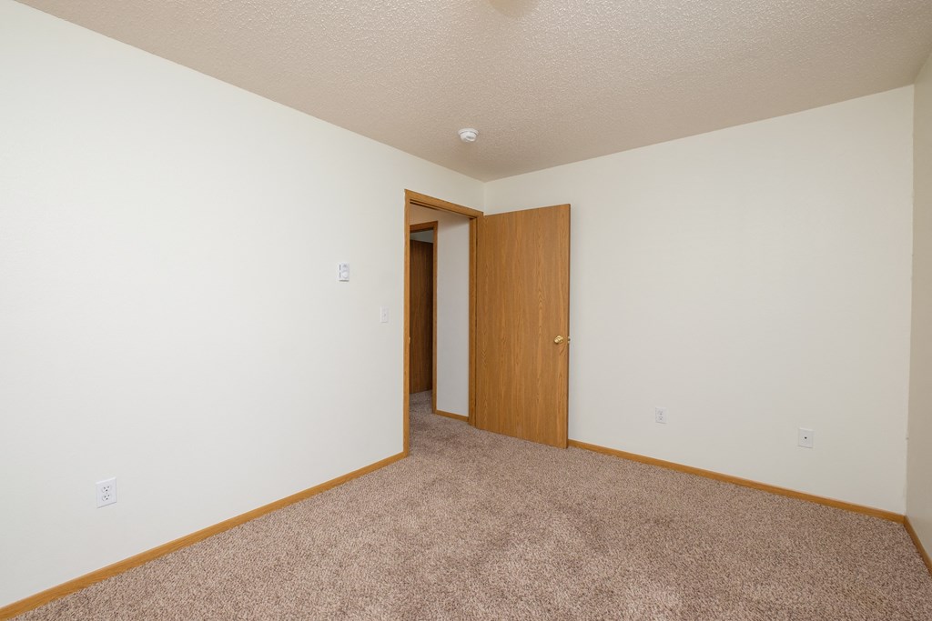 a room with a carpeted floor and a door to a closet. Fargo, ND Danbury Apartments