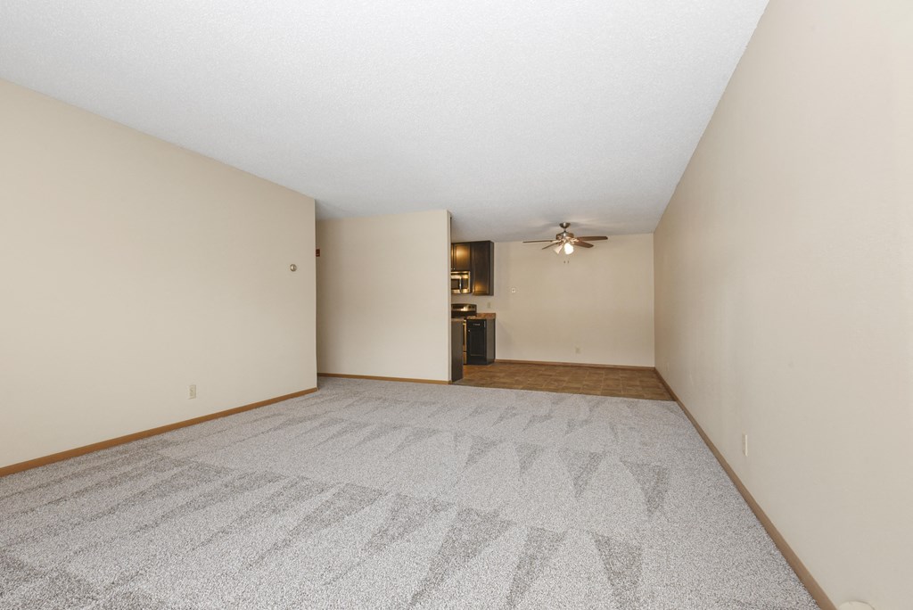 Anoka, MN Dellwood Estates Apartments. An empty living room with a ceiling fan and a kitchen in the background