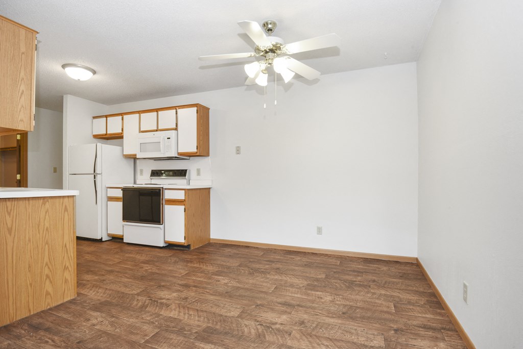 an empty living room with a kitchen and a ceiling fan