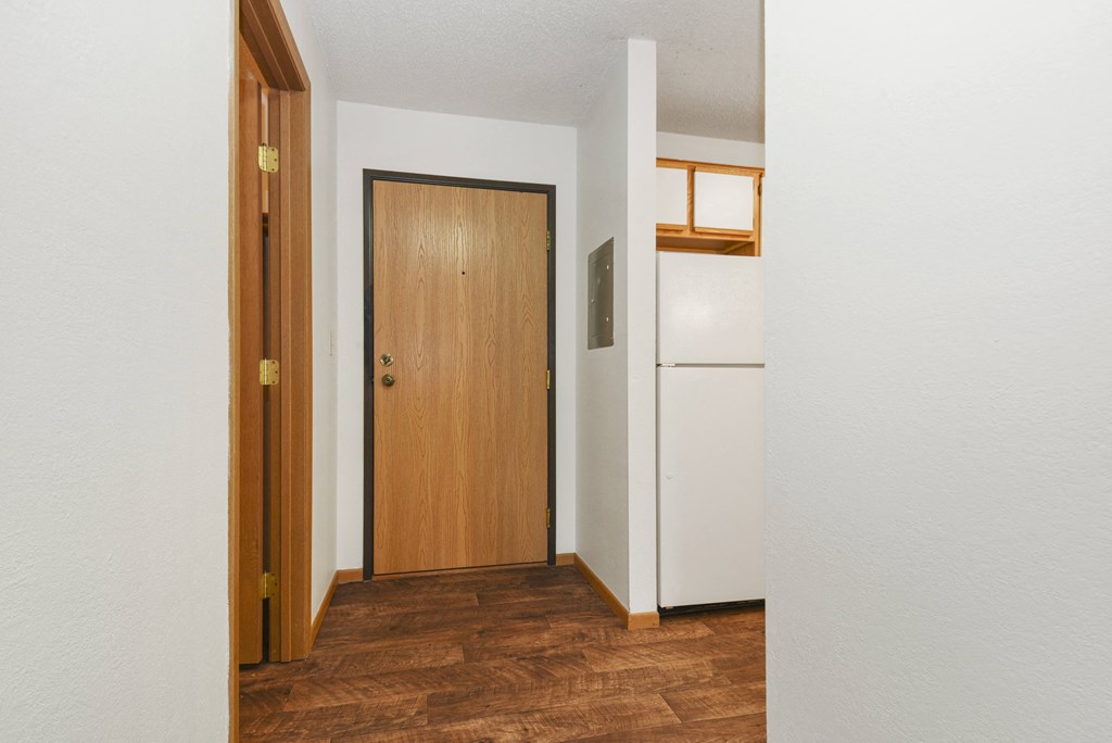 a hallway with a wooden door and a white refrigerator. Anoka, MN Dellwood Estates