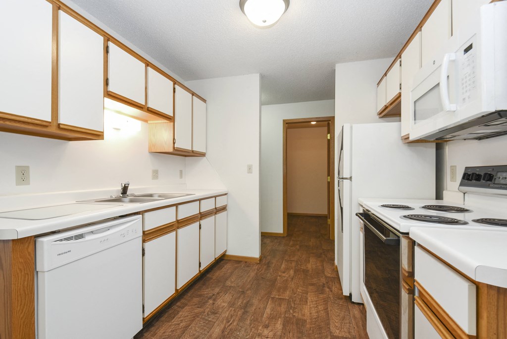 a kitchen with white appliances and wood flooring and white cabinets. Anoka, MN Dellwood Estates