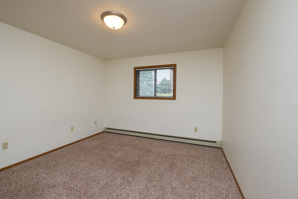 a bedroom with carpet and a window. Fargo, ND Dynasty Apartments
