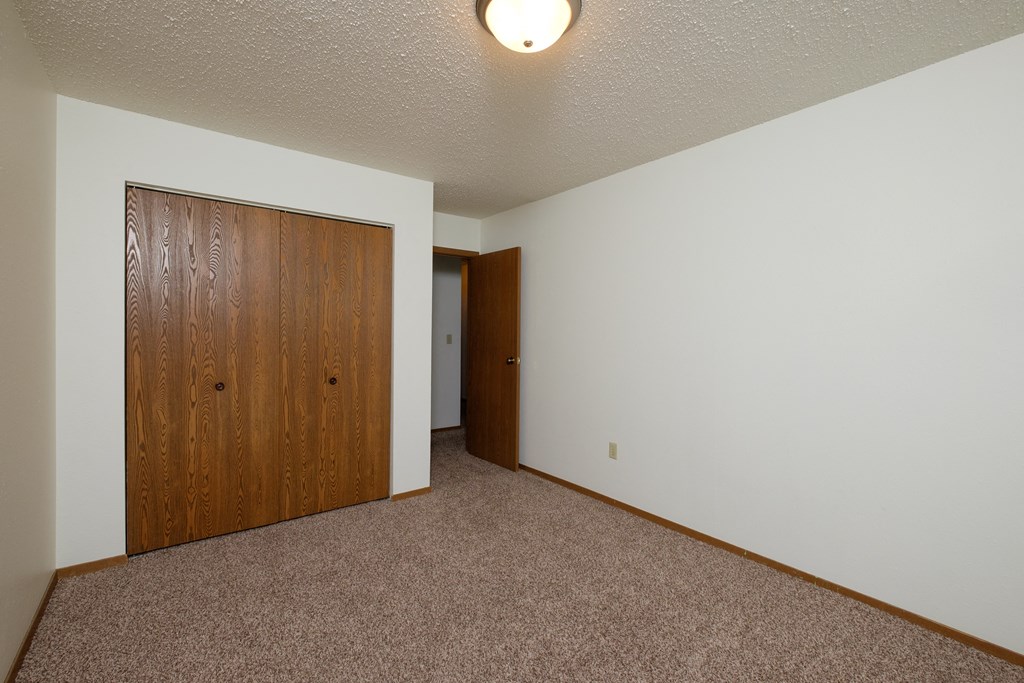 a bedroom with carpet and a door to a closet. Fargo, ND Dynasty Apartments