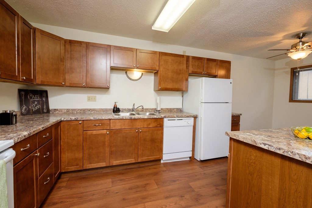 a kitchen with wooden cabinets and a white refrigerator. Fargo, ND Dynasty Apartments
