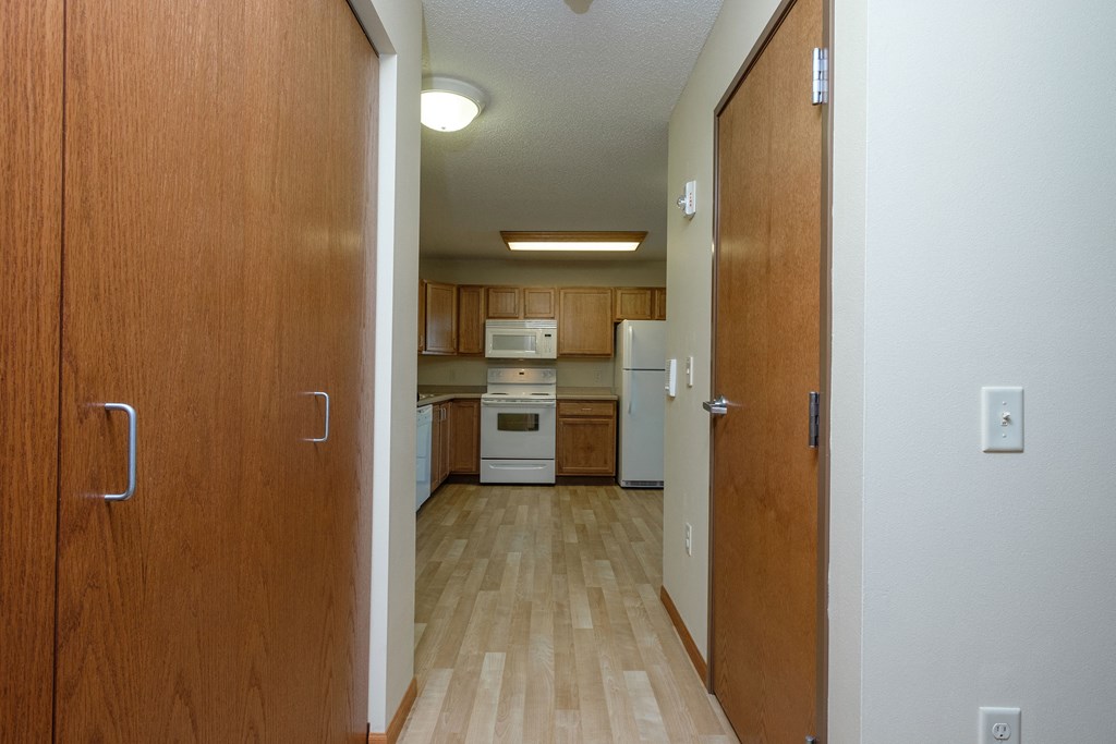 a hallway with closet doors and the kitchen in the background. Fargo, ND Crossroads Apartments