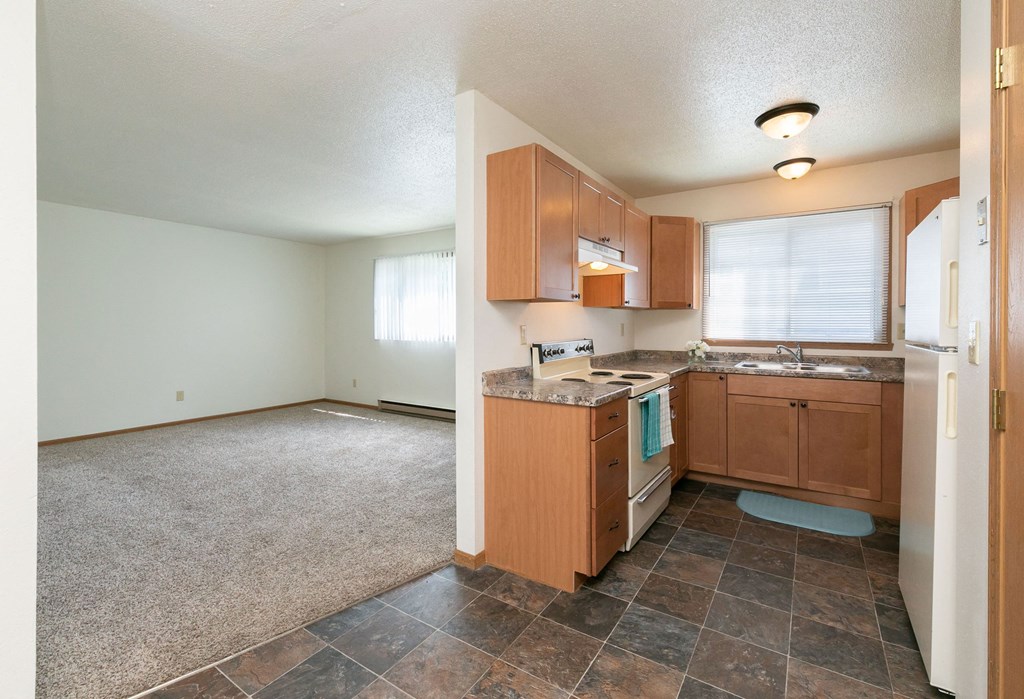 a kitchen with a window above the sink and a living room off to the side. Fargo, ND White Ridge Apartments
