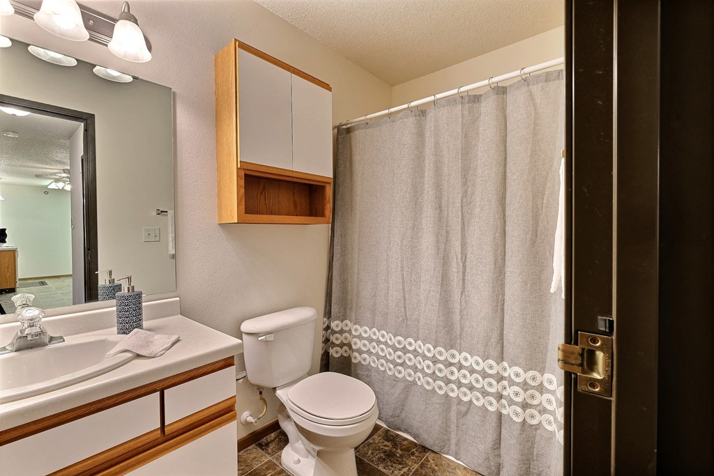 A bathroom with a shower toilet and sink and a mirror. Fargo, ND Eagle Run Apartments.