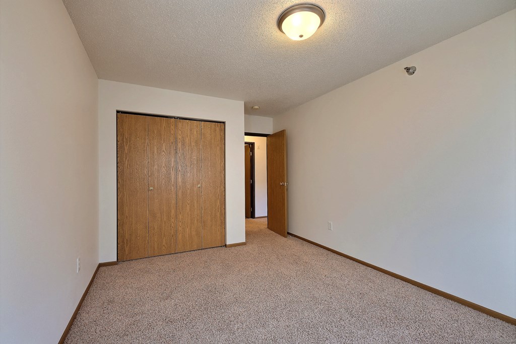 A spacious living room with carpet and a door to a bedroom. Fargo, ND Eagle Run Apartments.