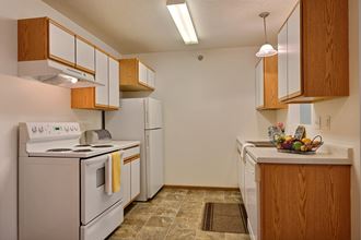 A kitchen with white appliances and wooden cabinets and a white refrigerator. Fargo, ND Eagle Run Apartments