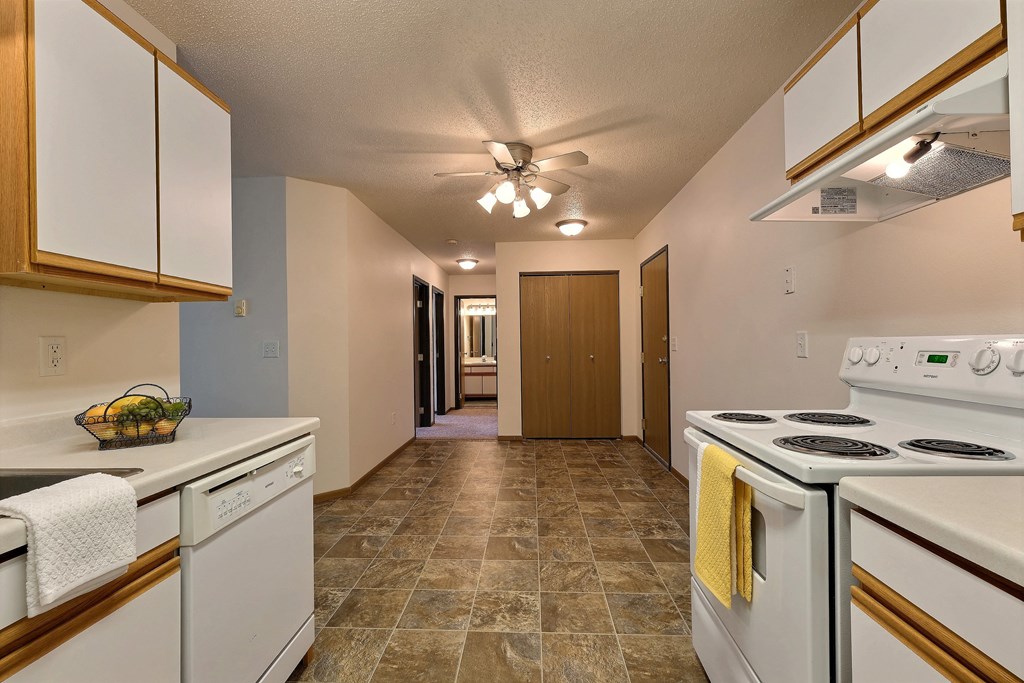 A kitchen with white appliances and white cabinets and a ceiling fan. Fargo, ND Eagle Run Apartments.