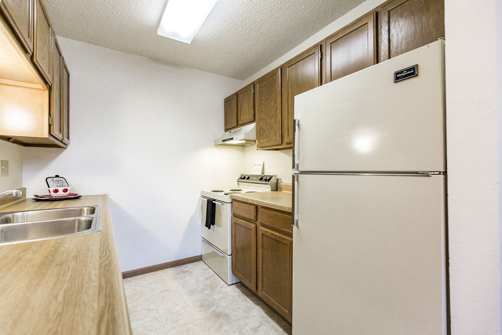 Bismarck, ND Eagle Sky II Apartments. A kitchen with a white refrigerator freezer next to a stove top oven